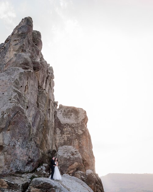 Pareja de novios está de pie cerca del alto acantilado y abrazándose, viaje de bodas, foto de la boda