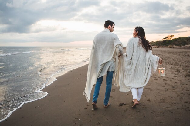 Pareja paseando por la playa con una vela