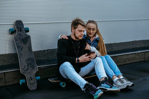 Pareja con patineta y smartphone al aire libre