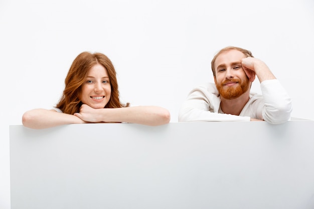 Pareja pelirroja escondiéndose detrás de la mesa, sonriendo