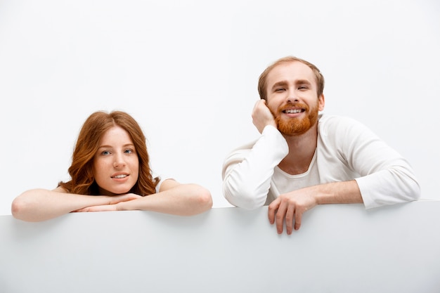 Pareja pelirroja escondiéndose detrás de la mesa, sonriendo