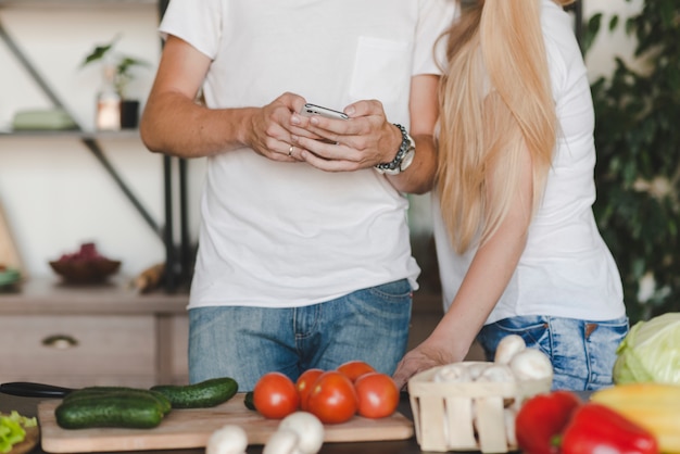 Pareja de pie detrás del mostrador de la cocina con teléfono móvil