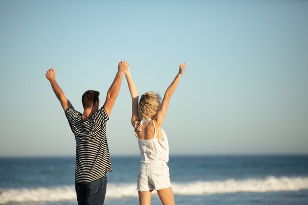 Pareja de pie junto con los brazos en la playa