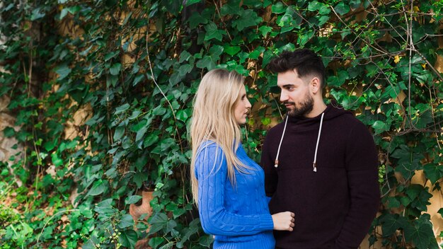 Pareja de pie junto a la pared con hojas verdes