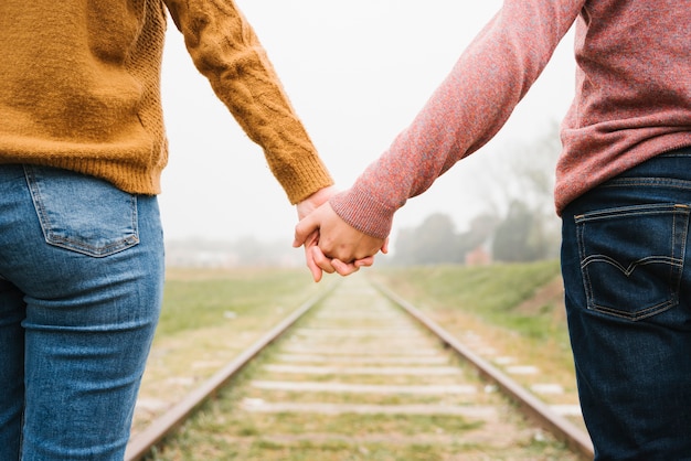 Pareja de pie en las vías del ferrocarril y tomados de la mano