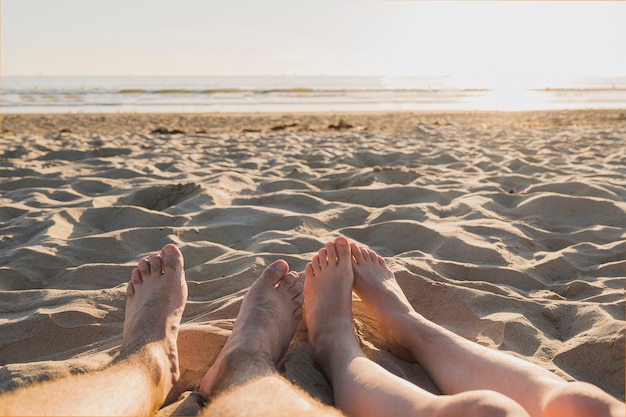 Pareja con los pies descalzos sobre la arena y el atardecer