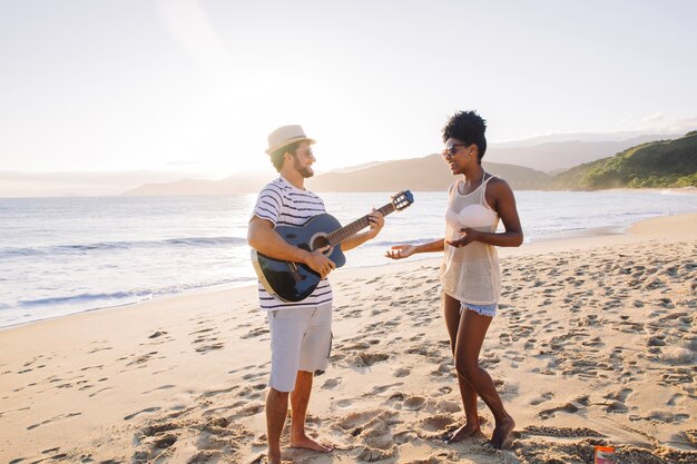 Pareja de pies en la playa tocando la guitarra