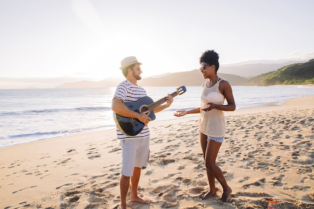 Pareja de pies en la playa tocando la guitarra