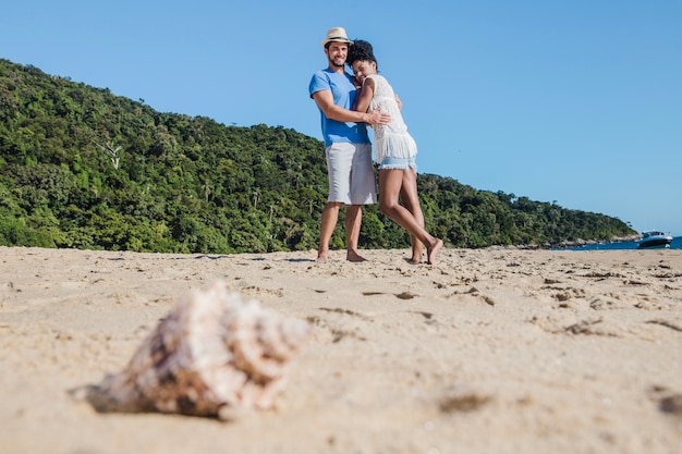 Pareja en la playa con concha en primer plano