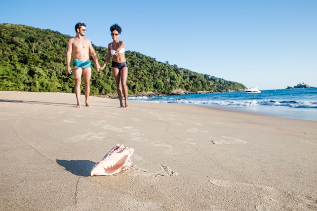 Pareja en la playa con concha en primer plano