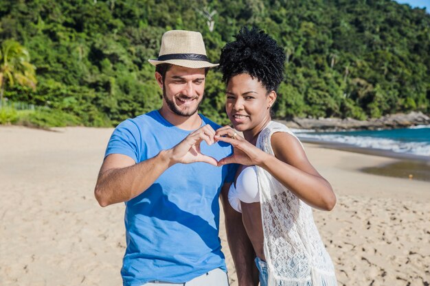 Pareja en la playa formando corazón con la manos