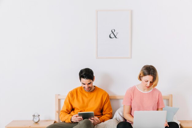 Pareja con portátil y tableta en la cama