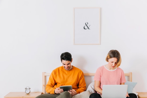 Pareja con portátil y tableta en la cama