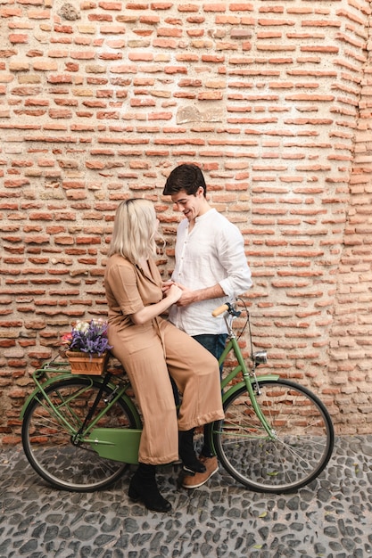 Pareja posando contra la pared de ladrillo con bicicleta