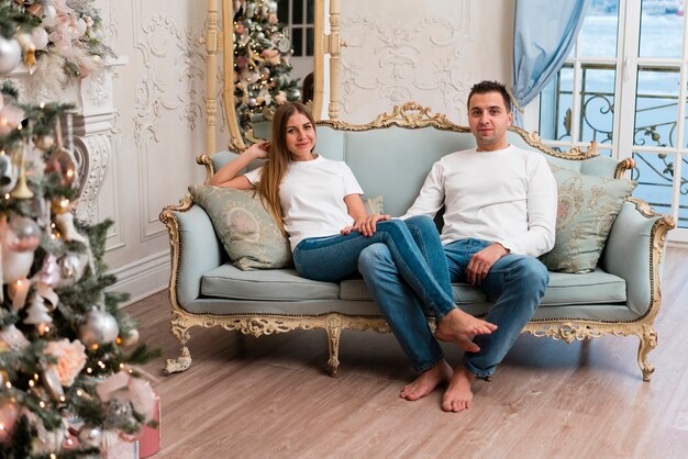 Pareja posando en el sofá con árbol de navidad