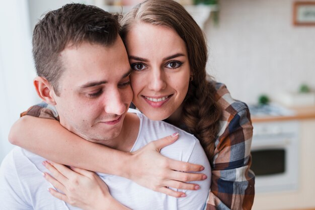 Pareja positiva abrazando cerca de la cocina en casa