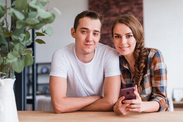 Pareja positiva con smartphone cerca de mesa en casa