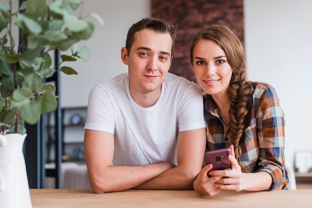 Pareja positiva con smartphone cerca de mesa en casa