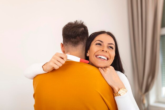 Pareja con prueba de embarazo casera positiva Estoy embarazada Pareja joven feliz con prueba de embarazo Primer plano de una mujer joven feliz abrazando a un hombre después de una prueba de embarazo positiva