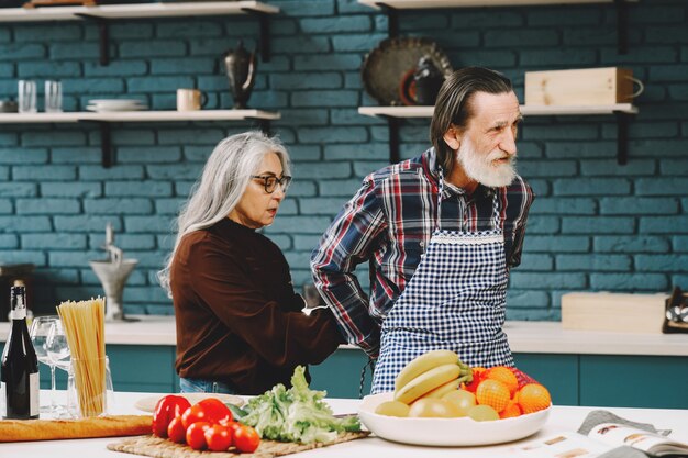 Pareja de raza europea senior poniéndose delantales en la cocina