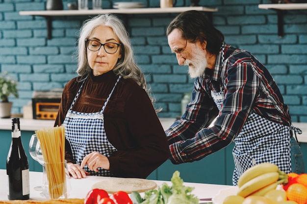 Pareja de raza europea senior poniéndose delantales en la cocina