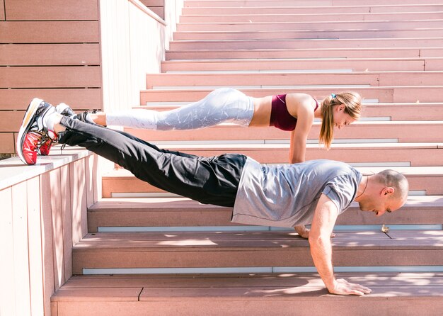 Foto gratuita pareja realizando empuje hacia arriba el ejercicio en la escalera en la luz del sol