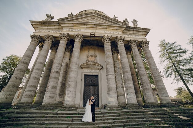 Pareja de recién casados besándose con edificio antiguo de fondo