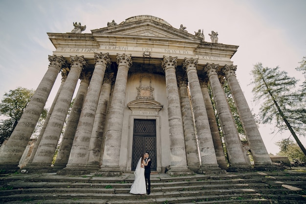 Pareja de recién casados besándose con edificio antiguo de fondo