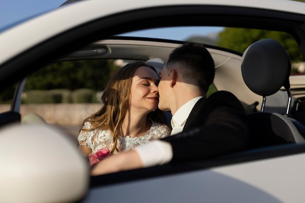 Una pareja de recién casados besándose junto a un auto pequeño