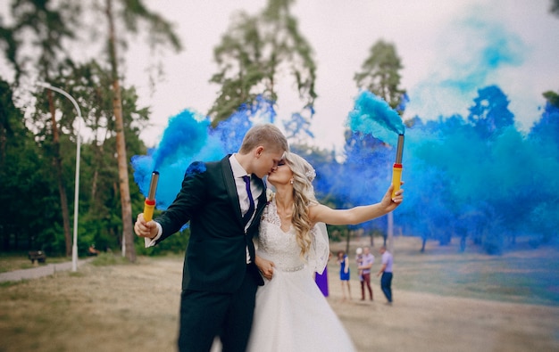 Foto gratuita pareja de recién casados besándose y sujetando bengalas azules