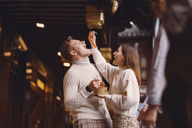 Pareja de recién casados comiendo fideos con palillos en Shanghai fuera de un mercado de alimentos