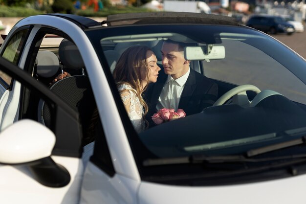 Una pareja de recién casados dentro de un auto pequeño