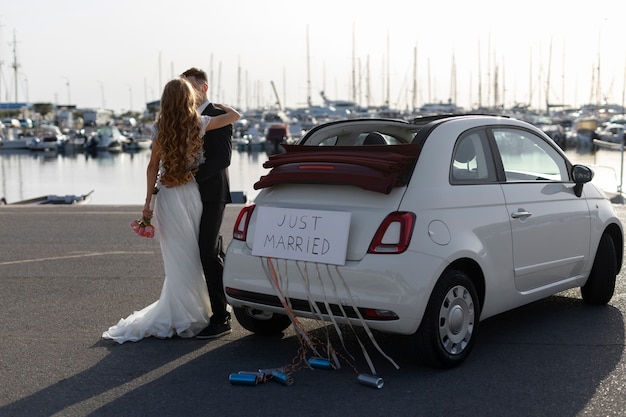 Una pareja de recién casados junto a un auto pequeño