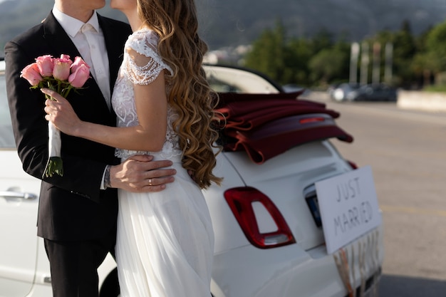 Una pareja de recién casados junto a un auto pequeño