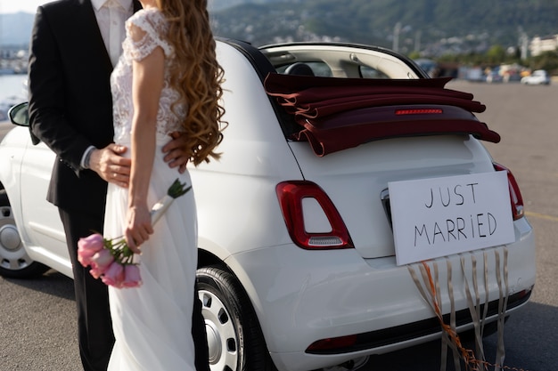 Foto gratuita una pareja de recién casados junto a un auto pequeño