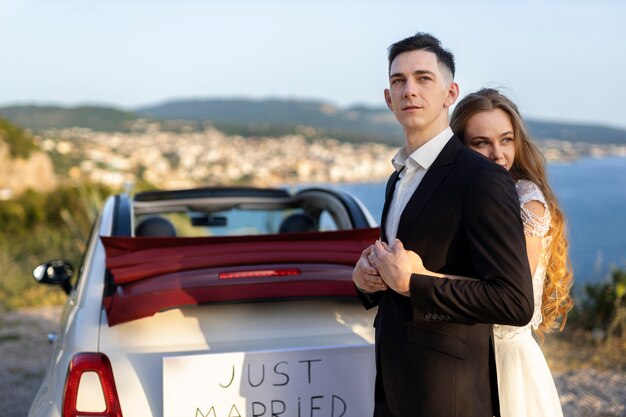 Una pareja de recién casados junto a un auto pequeño