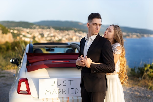 Foto gratuita una pareja de recién casados junto a un auto pequeño