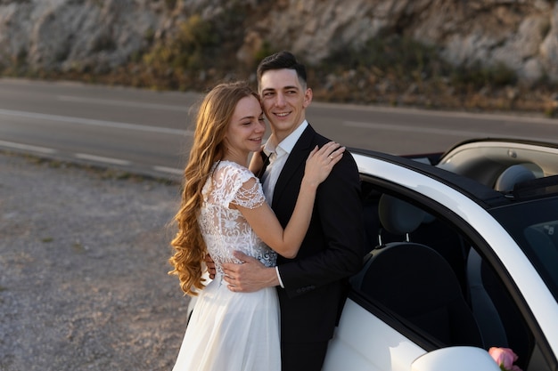 Una pareja de recién casados junto a un auto pequeño