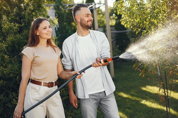 Pareja regando sus plantas en su jardín. Hombre con camisa azul. La familia trabaja en un patio trasero.