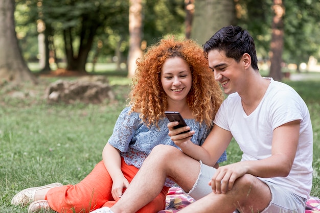 Pareja revisando celular en el parque y divirtiéndose