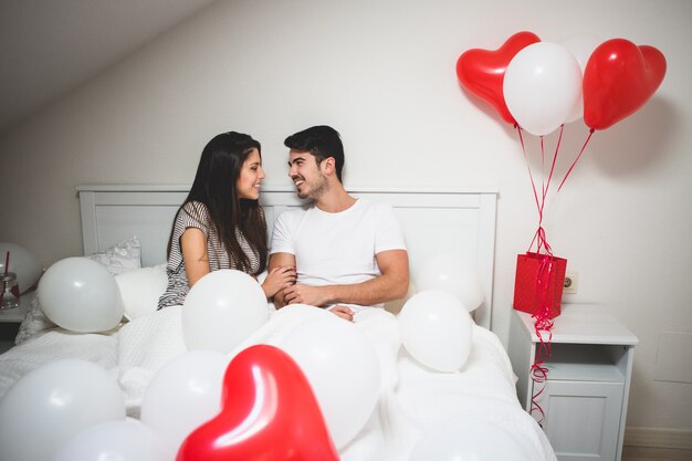 Pareja riendo tumbada en la cama con globos a su alrededor