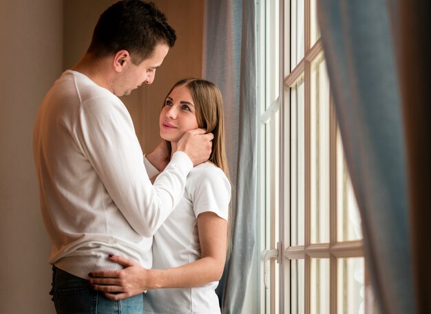 Pareja romántica abrazada junto a la ventana