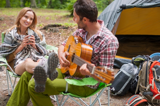 Pareja romántica en un camping. Hombre tocando la guitarra.