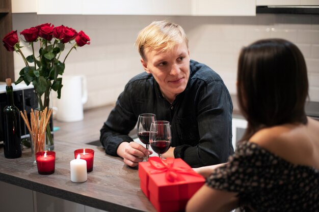 Pareja romántica celebrando el día de San Valentín en casa con vino y presente