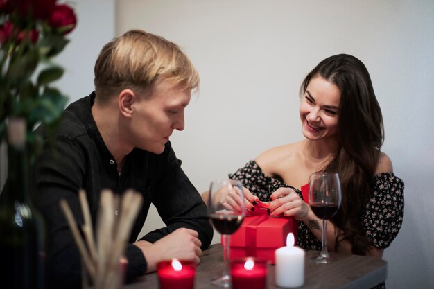 Pareja romántica celebrando el día de San Valentín en casa con vino y presente