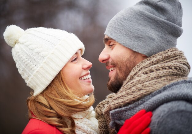 Pareja romántica con gorros de lana y mirándose el uno al otro