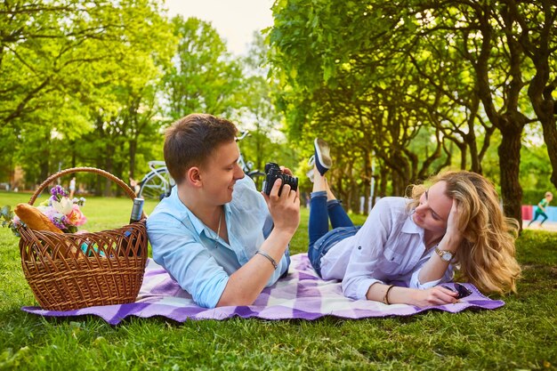 Pareja romántica haciendo fotos en tiempo de picnic en un parque.