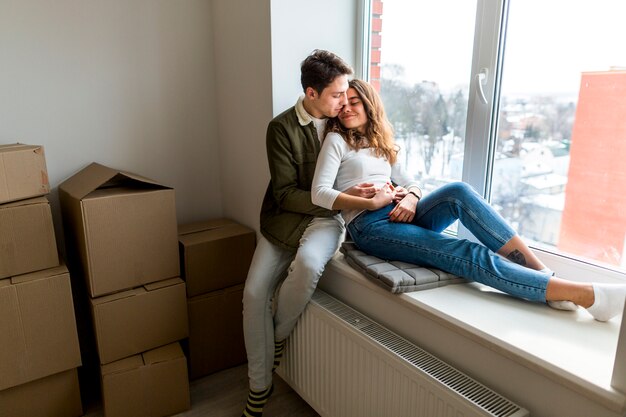 Pareja romántica joven sentada en el alféizar de la ventana en su nuevo apartamento