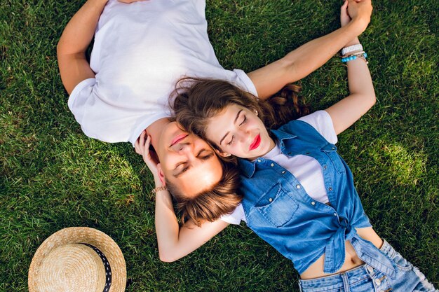 Pareja romántica de jóvenes tumbados en la hierba en el parque. Se recuestan sobre los hombros y se toman de las manos. Mantienen los ojos cerrados y se ven relajados. Vista desde arriba.