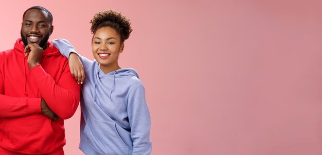 Una pareja romántica mejores amigas de pie con fondo rosa chica apoyándose en el hombro del novio sonriendo